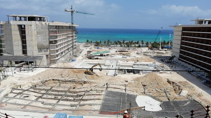 Secrets Moxché en obra: las torres en obra gris, la grúa y la alberca en cimentación con el mar al fondo